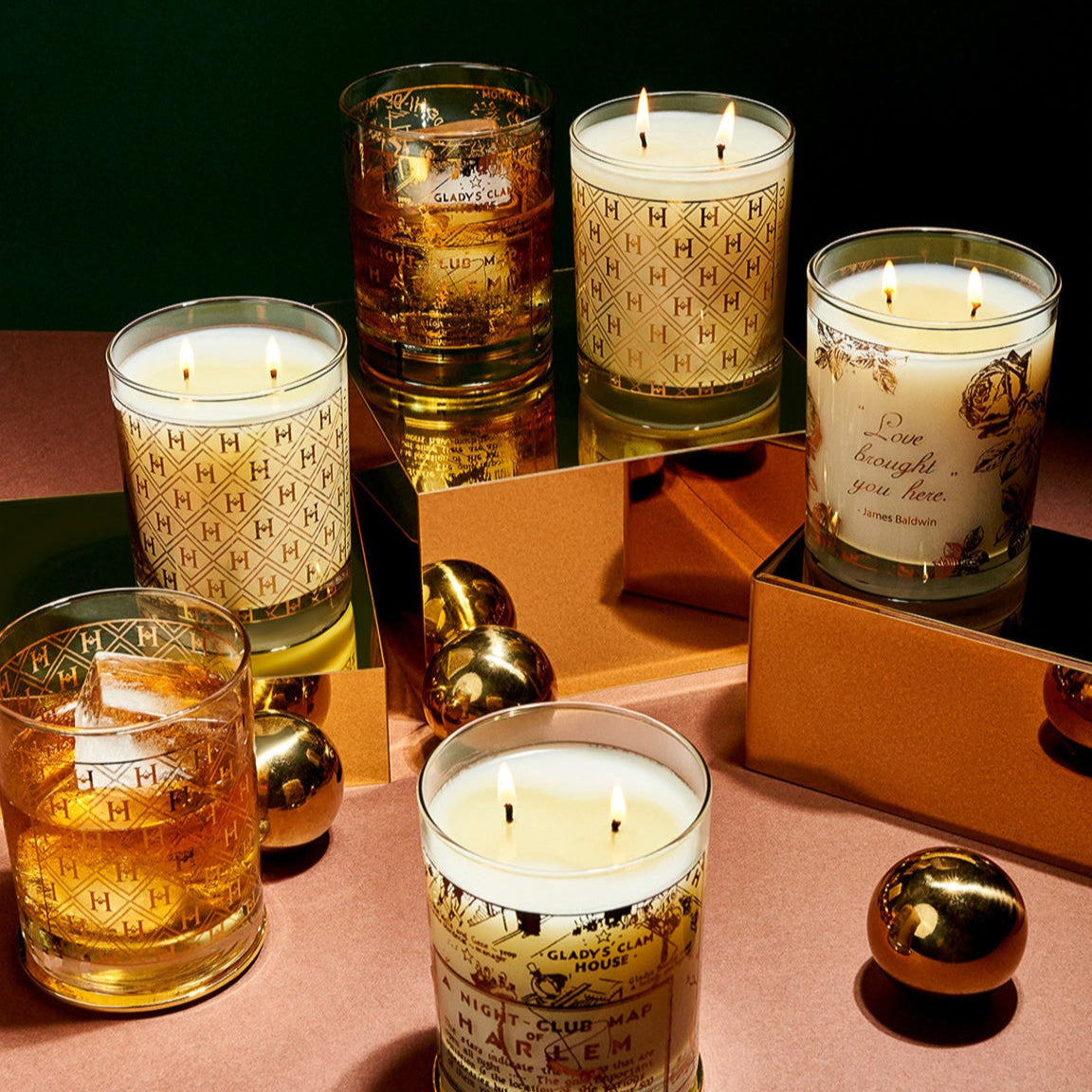 Collection of lit candles in glass containers on a reflective surface with a dark background