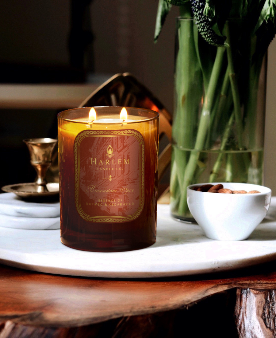 Brownstone Spice Candle on a white tray with greenery, a gold candle holder, and a small bowl of almonds.