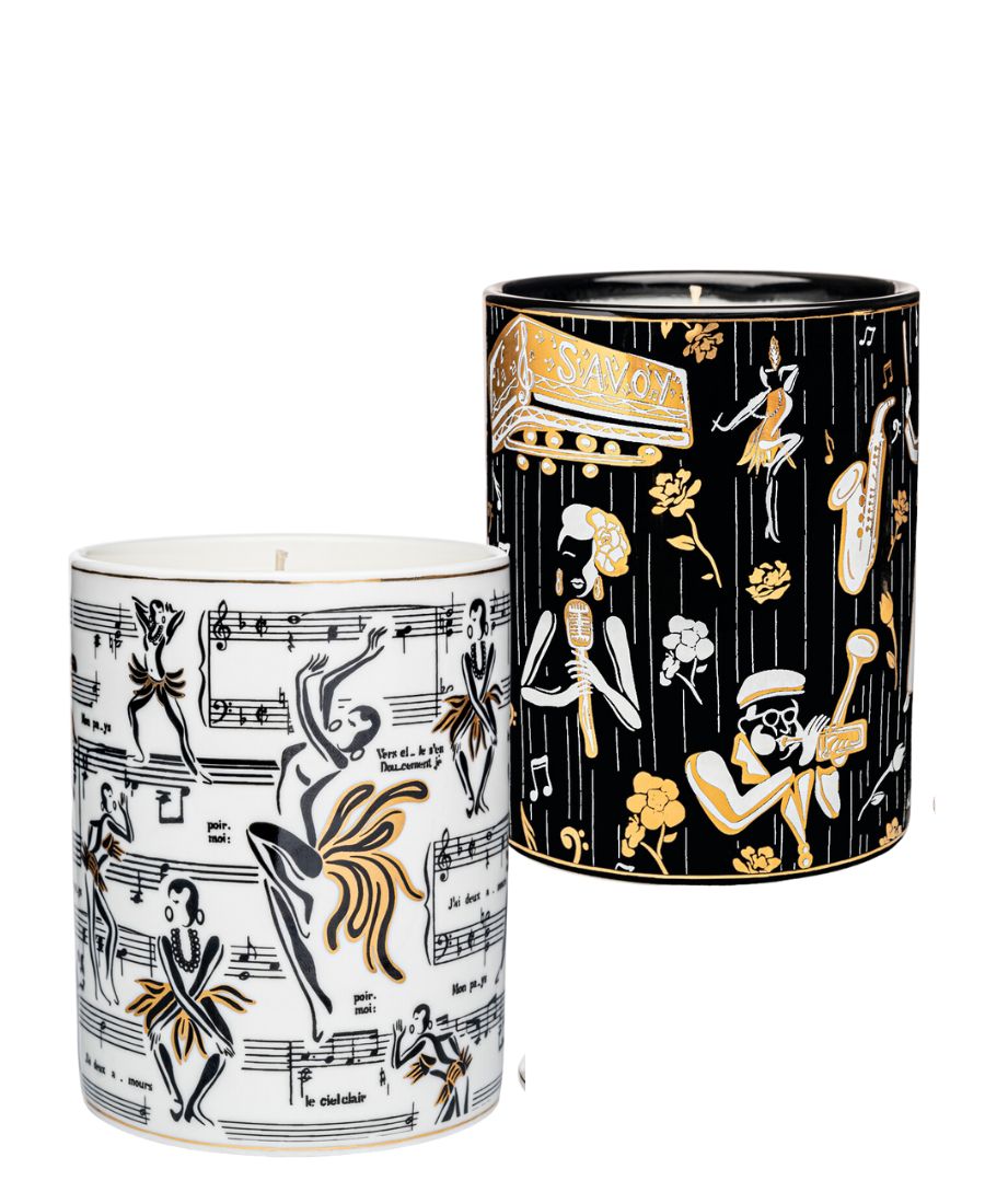 This is an image of our gold and white Deux Amours ceramic candle with a lid. It features illustrations of Josephine Baker, and other original illustrations. The back of the candle has the words Harlem Candle Co on the vessel in gold and black. It is pictured next to our Duke ceramic candle with illustrations of Billie Holiday, Dizzy Gillespe, and other symbols of jazz.