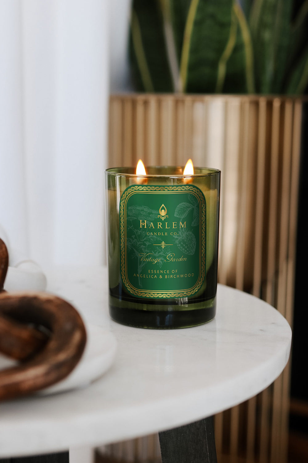 This is a lifestyle image of our vintage garden candle on a white marble table next to a plant and decorative items.