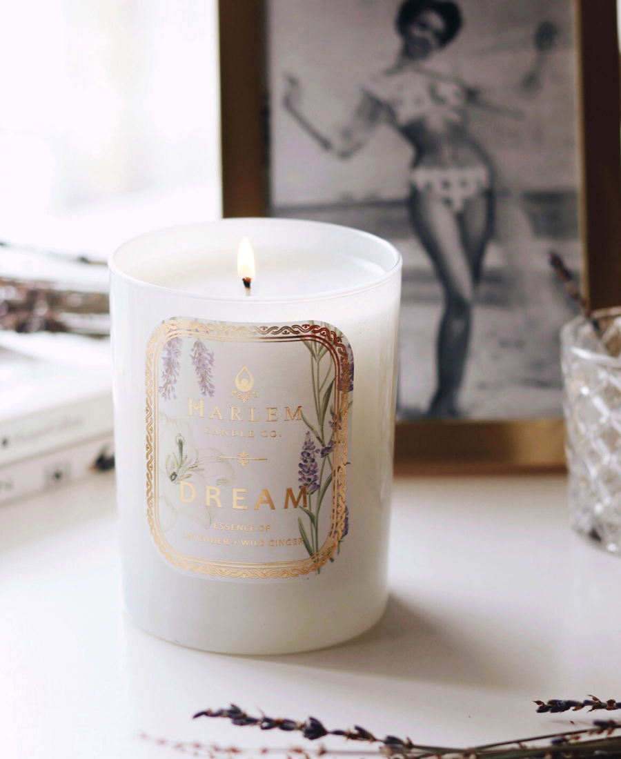 Dream Candle on a white table with a gold framed vintage photograph of a woman, glassware, and flowers.