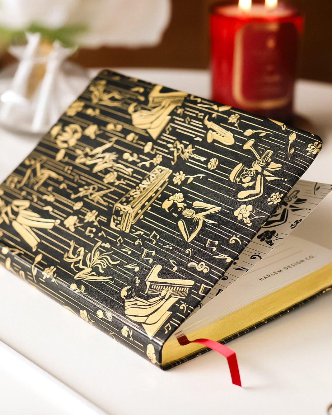 This is a lifestyle image of the black and gold owed to the Harlem Renaissance journal that features illustrations of Billie Holiday, Duke Ellington, dizzy, Gillespie, and Cab Calloway.
