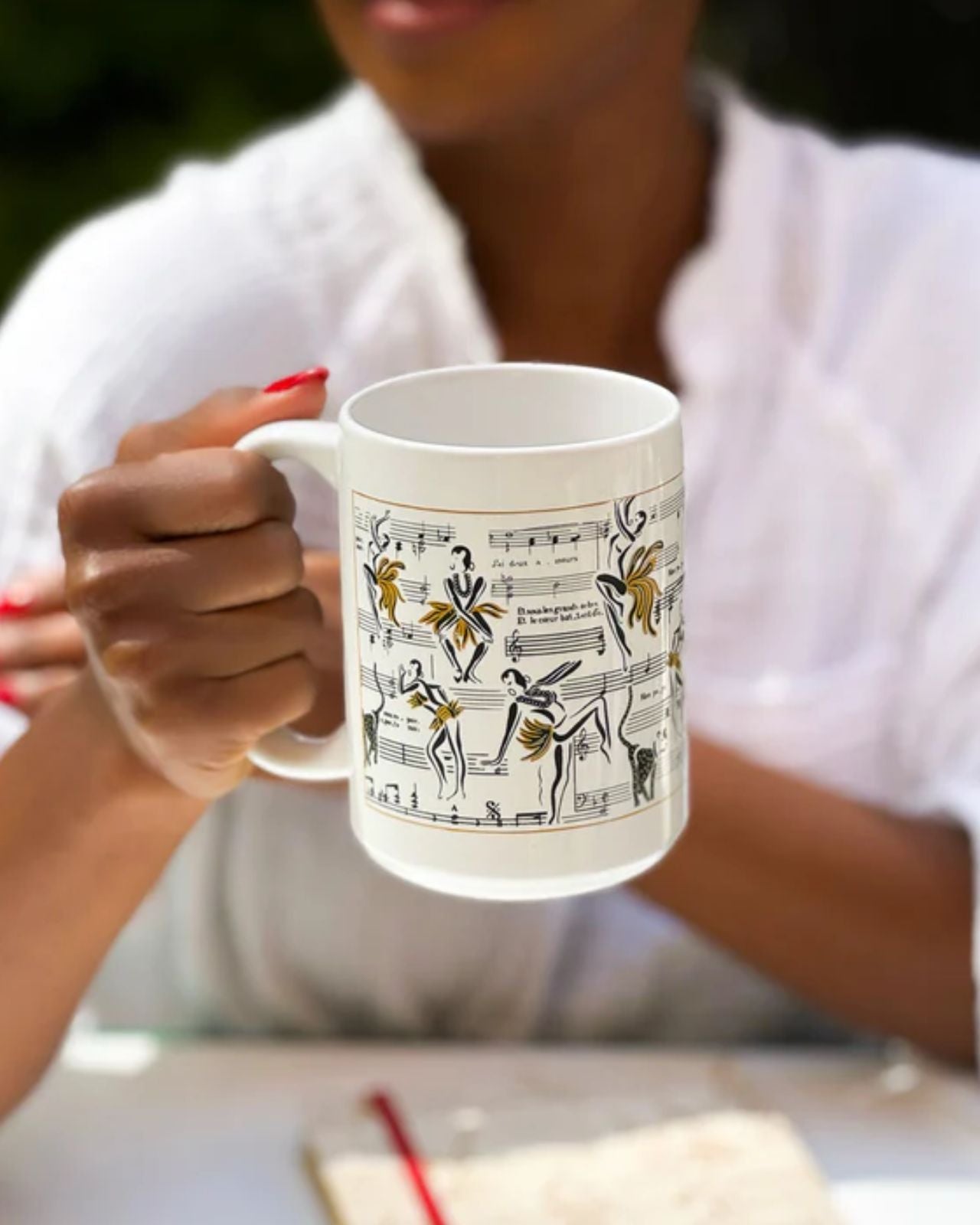 This is an image of our Josephine coffee mug with the similar design as our Deux Amour candle and Ode to Josephine journal.  The mug is being held by a model with red finger nails.