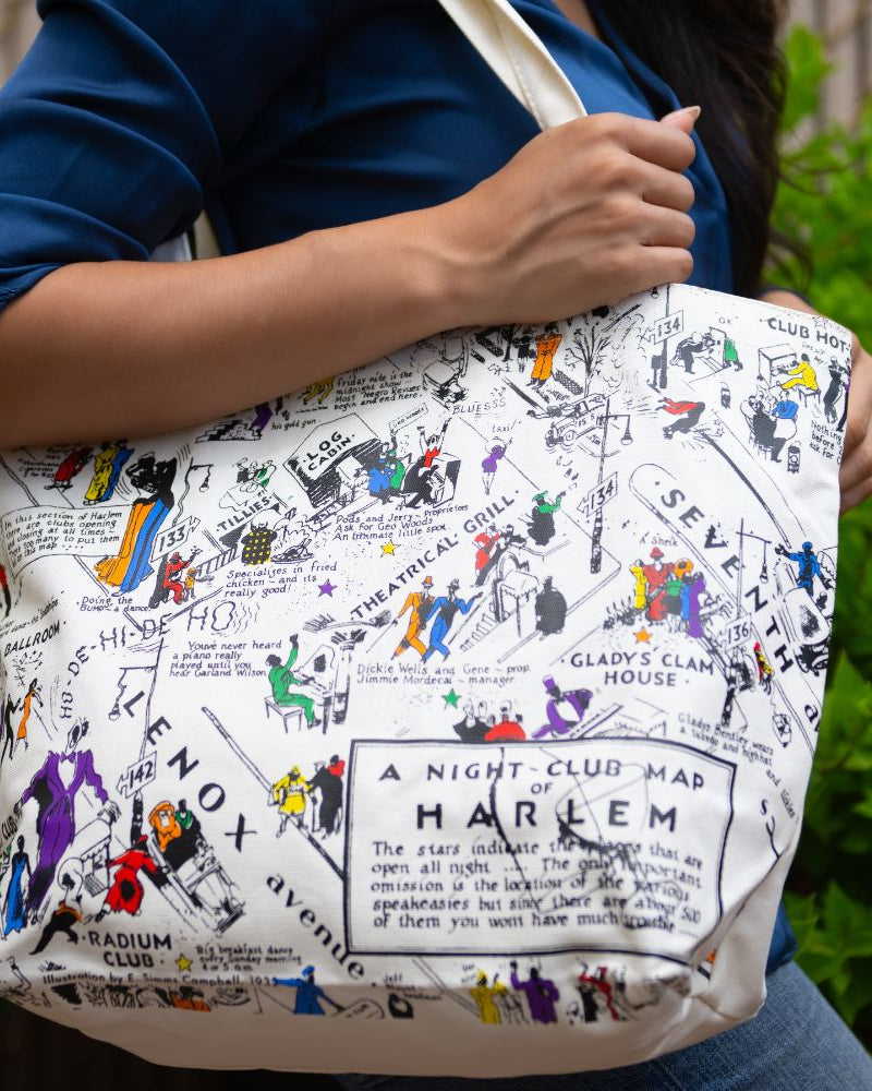 Person holding a tote bag with a colorful map design of Harlem, New York.
